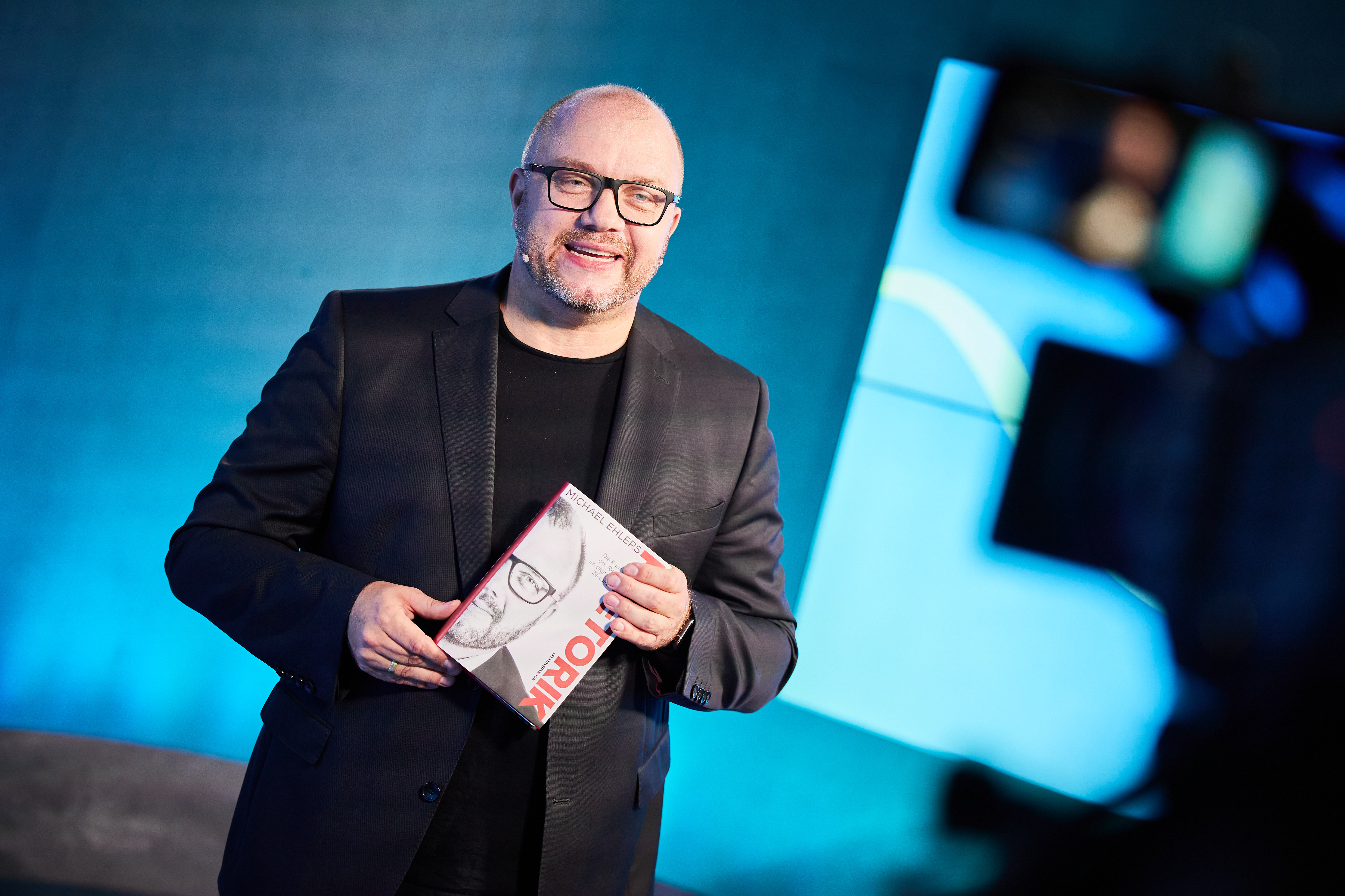 Michael Ehlers mit seinem Buch Rhetorik vor blauem Bühnenhintergrund